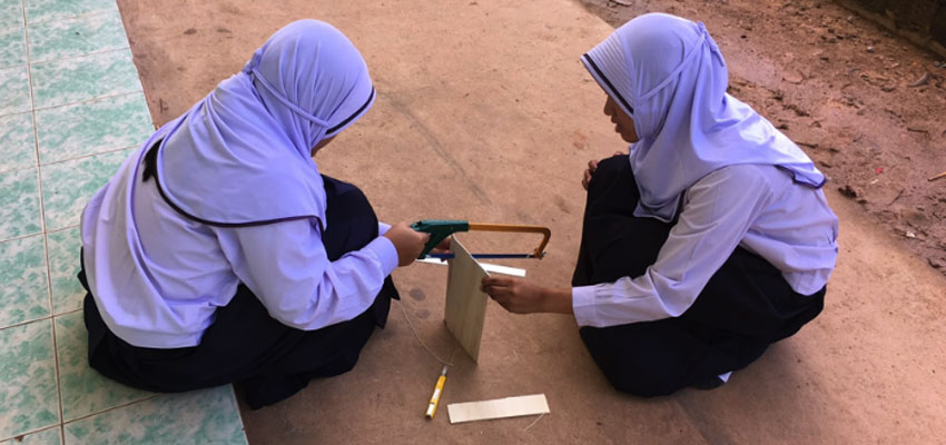 Two students sawing outside to build their prototype in Ao Kapor.