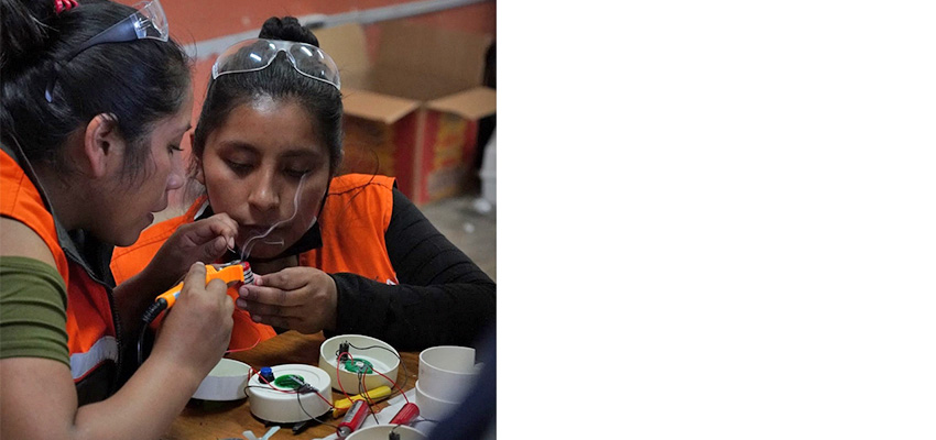 Two women sitting close togegther working on a small technical task.
