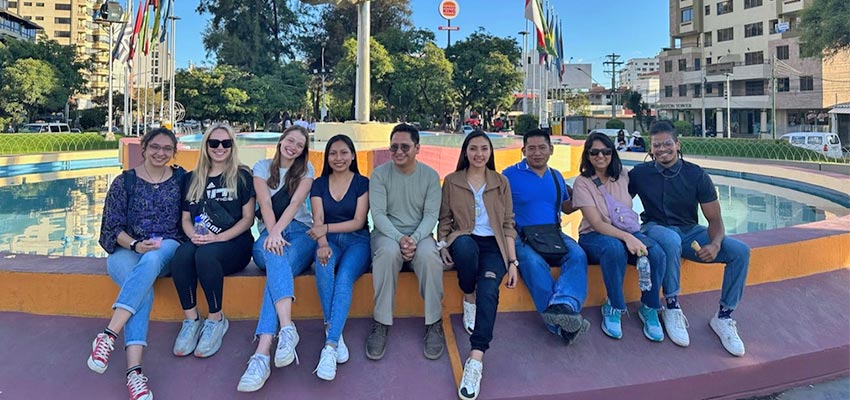 Nine adults seated at the edge of a fountain.
