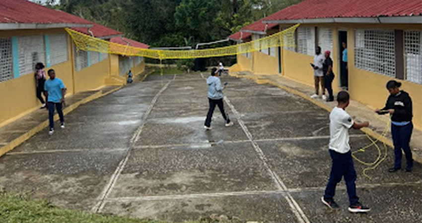 A small group of young people in a courtyard playing volleyball using a yellow net.