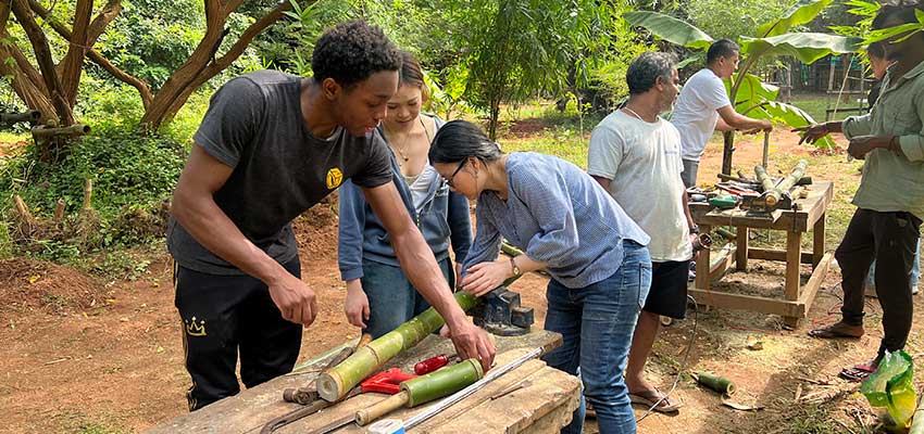 Three people standing on either side of a work table outside sawing.