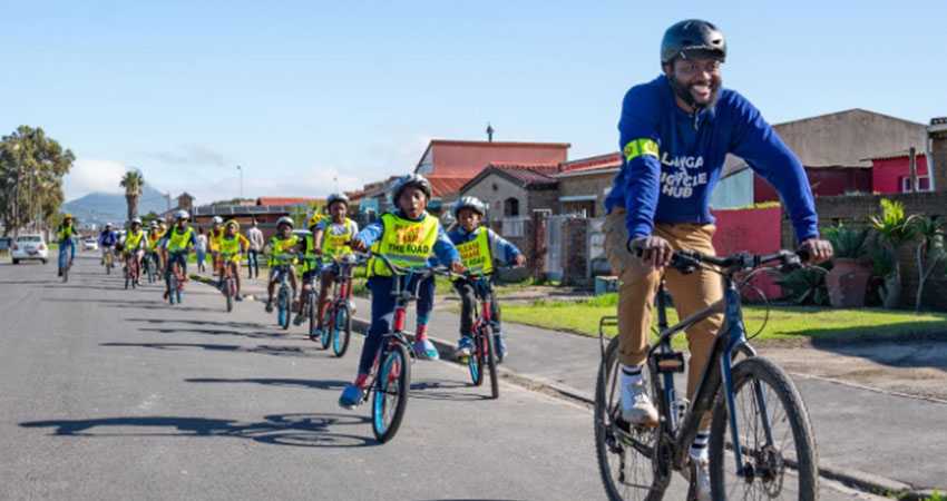 A dozen are more people riding bicycles in a line on a street.