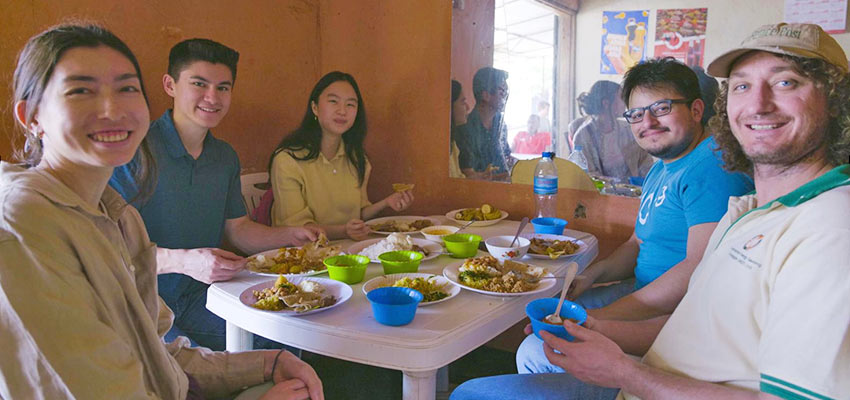 Five people sitting around a white table sharing a meal.
